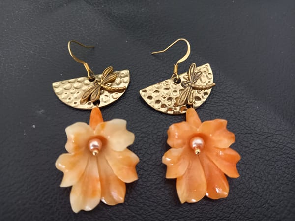 20250129_135046 Boucles d’oreilles avec fleur de corail orange suspendue, demi-cercle doré martelé et libellule.