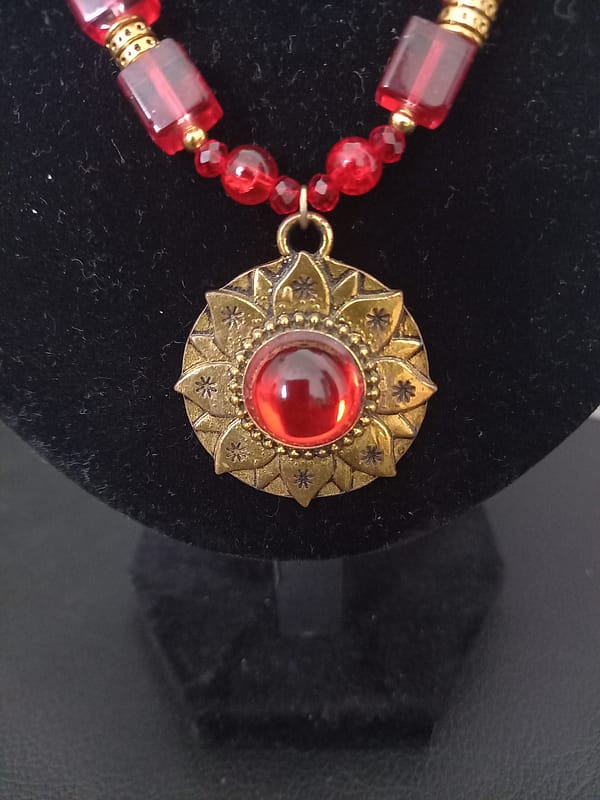 20250120_144614 Collier rouge avec pendentif soleil doré et cabochon rouge, perles de verre rouges et perles tibétaines dorées.