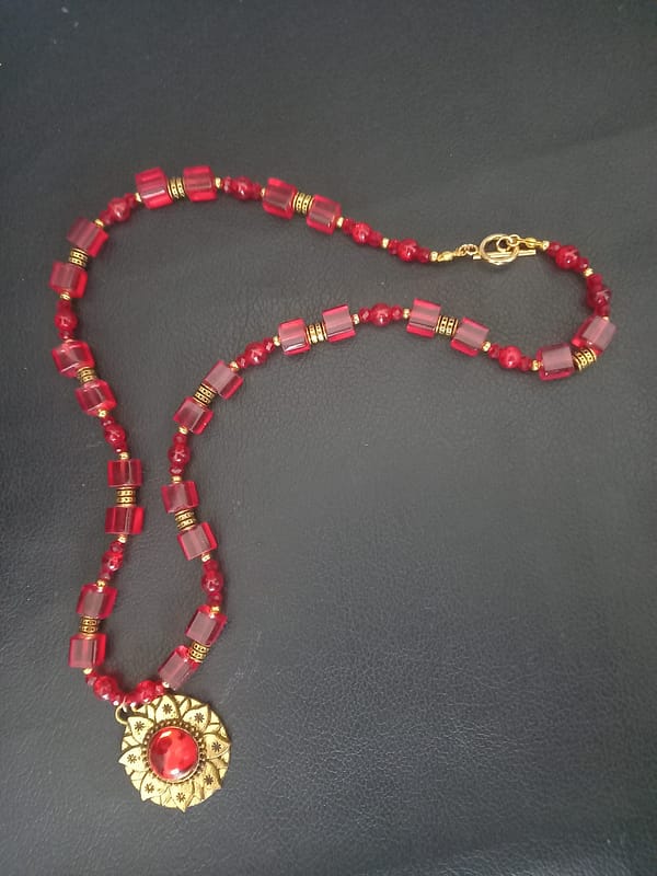 20250120_144652 Collier rouge avec pendentif soleil doré et cabochon rouge, perles de verre rouges et perles tibétaines dorées.