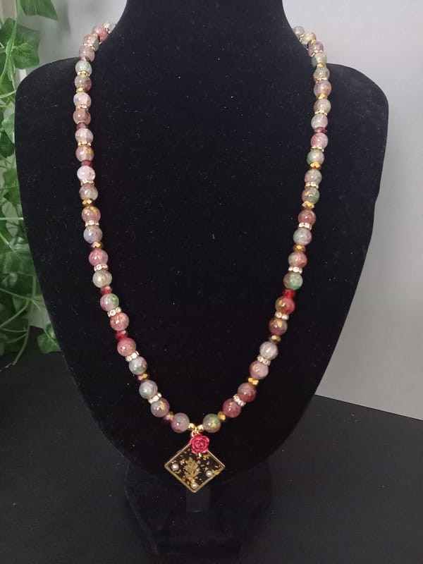20250120_144733 Collier en perles marbrées craquelées rouges et vertes, séparées de strass et perles dorées, avec pendentif losange à feuille d’or et rose rouge.