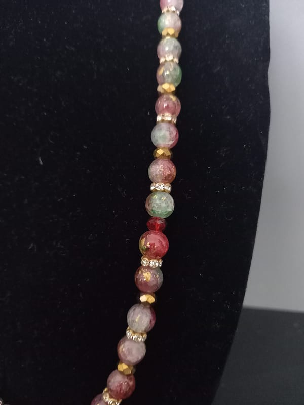 20250120_144753 Collier en perles marbrées craquelées rouges et vertes, séparées de strass et perles dorées, avec pendentif losange à feuille d’or et rose rouge.